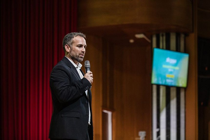 Santi García Cremades dando una conferencia con micrófono de mano ante un telón rojo